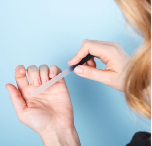 A manicurist filing a client's nails against a pale blue background