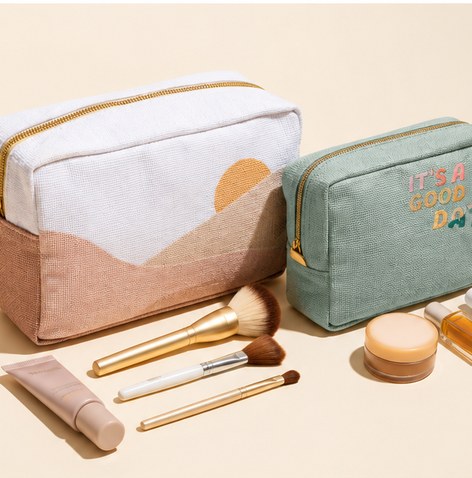 Two branded cosmetic pouches with make-up brushes and a compact on a cream background