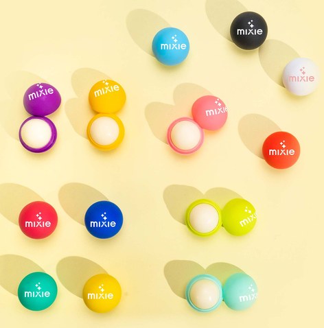 Dozens of round branded lip balm pots in assorted colours arranged on a pale yellow background